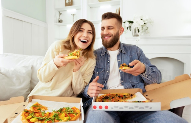 Un couple joyeux mangeant de la pizza devant la télévision en regardant un film comique.