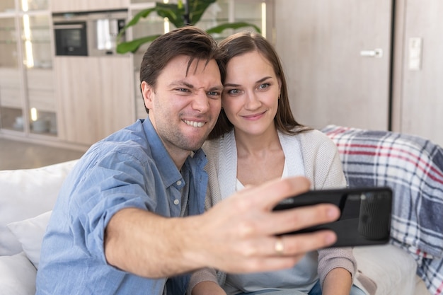 Un couple joyeux prend un selfie assis sur le canapé à la maison