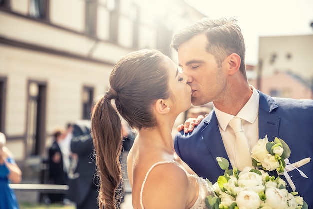Un couple juste marié s'embrassant devant l'église après le mariage et tenant un joli bouquet fait de belles fleurs.