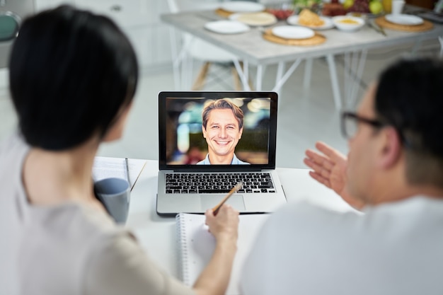 Couple latin prenant des notes tout en passant un appel vidéo à l'aide d'un ordinateur portable, contactant le client, parlant sur webcam. Notion de consultation en ligne. Focus sur l'écran d'ordinateur portable