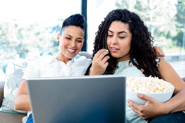 Couple de lesbiennes ayant pop-corn tout en utilisant un ordinateur portable dans le salon