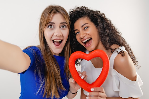 Couple de lesbiennes faisant selfie avec figure en forme de coeur rouge isolé