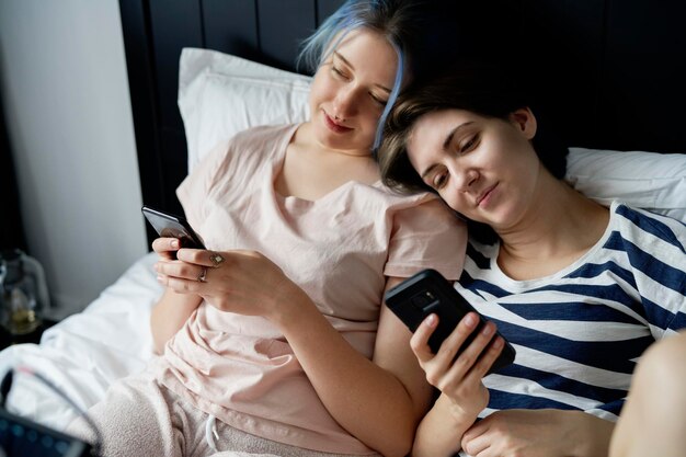 Un couple de lesbiennes romantiques allongés dans le lit avec des téléphones portables.