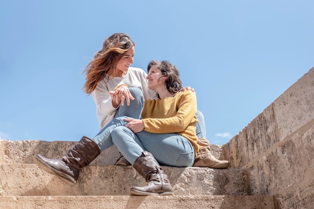 Un couple de lesbiennes s'embrassant et se regardant dans les yeux assis sur les escaliers en arrière-plan concept de ciel bleu du concept de mode de vie de relation de bisexualité Lgbt