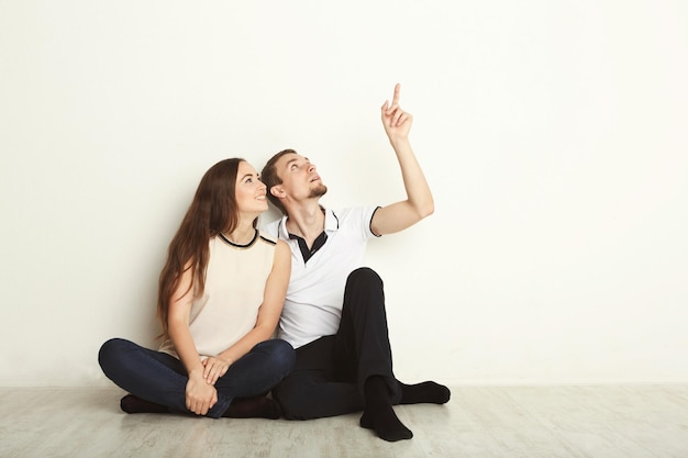 Couple levant les yeux, assis sur le sol dans un nouvel appartement, rêvant de l'avenir, l'homme pointe vers le haut, copiez l'espace