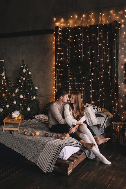 Couple sur le lit dans la chambre. Intérieur sombre. Nouvel An et Noël. Câlins et bisous. Amour. Pull blanc et chaussettes hautes. Rencontre amoureuse. Un amoureux des rendez-vous.