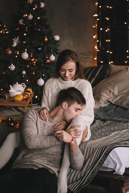 Couple sur le lit dans la chambre. Intérieur sombre. Nouvel An et Noël. Câlins et bisous. Amour. Pull blanc et chaussettes hautes. Rencontre amoureuse. Un amoureux des rendez-vous.