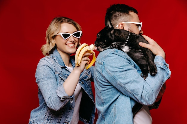 couple à lunettes de soleil sur fond rouge nourrir chien français avec banane couple heureux