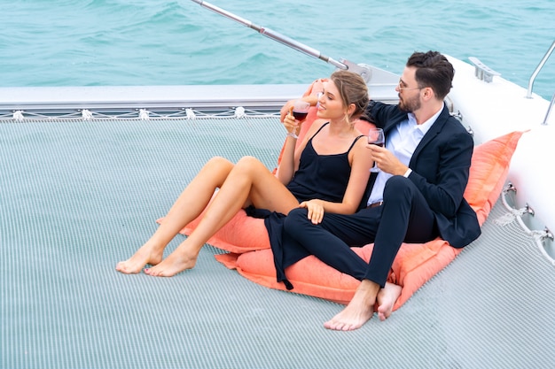 Un couple de luxe se détend en couple dans une belle robe et une suite est assis sur un sac de haricots et boit un verre de vin dans une partie du yacht de croisière.