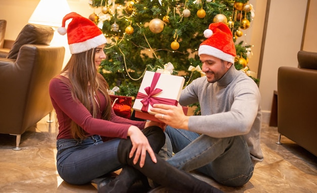 Couple à la maison pour Noël avec des gits et un arbre de Noël