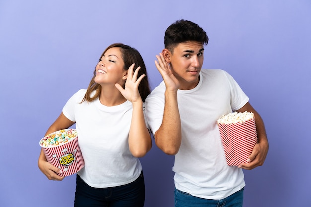 Couple de manger du pop-corn tout en regardant un film sur violet en écoutant quelque chose en mettant la main sur l'oreille
