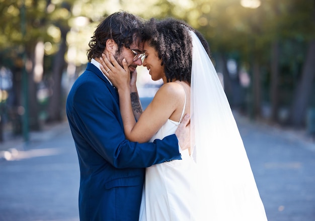 Couple de mariage et amour en plein air pour l'événement de célébration de mariage avec engagement Heureux homme et femme interracial au parc avec partenariat de confiance et sourire tout en touchant le visage avec soin