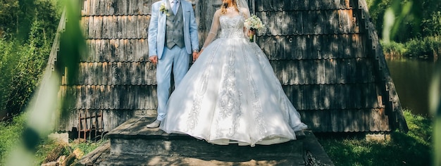 Couple de mariage amoureux se promène à l'extérieur Le marié en costume bleu et la mariée en robe de luxe sont près du mur en bois Beau bouquet dans les mains Style rustique