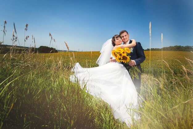 Couple de mariage dans le champ d'été avec bouquet de tournesols