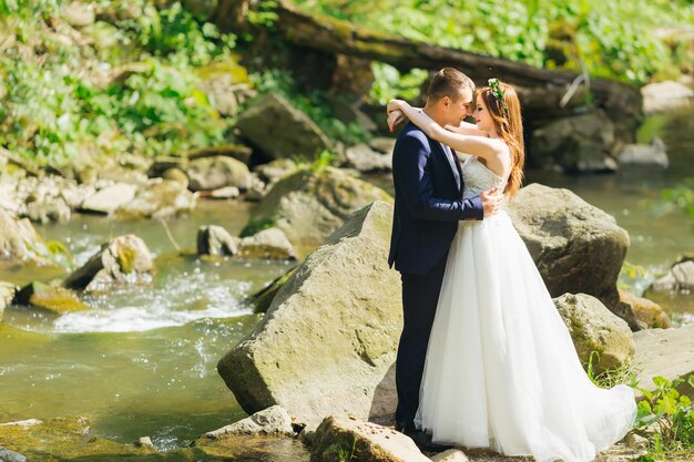 couple de mariage debout sur les pierres au bord de l'eau