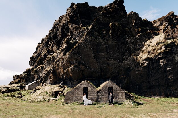 Couple de mariage posant dans les vieilles maisons couvertes de mousse sur le fond d'une montagne rocheuse