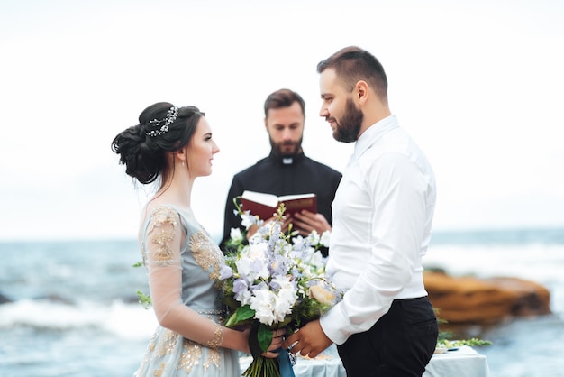 Couple de mariage près de l'océan avec un prêtre