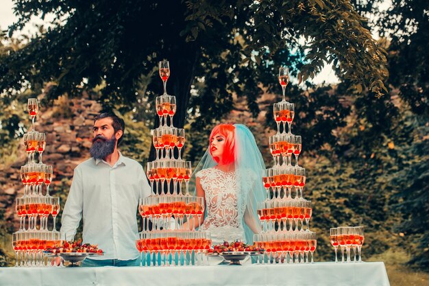 Photo couple de mariage avec des pyramides de verres à vin en plein air