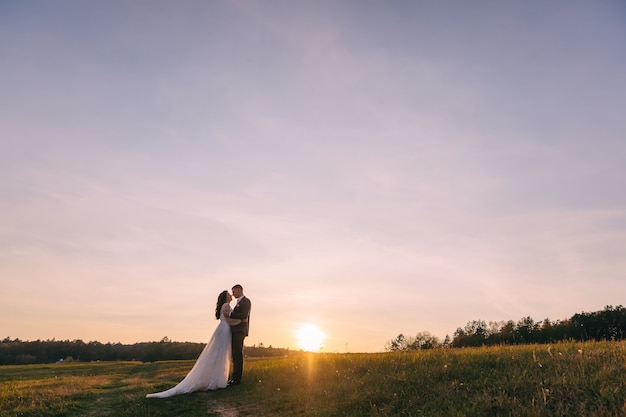 Couple de mariage romantique posant au sommet des montagnes au coucher du soleil avec une vue imprenable