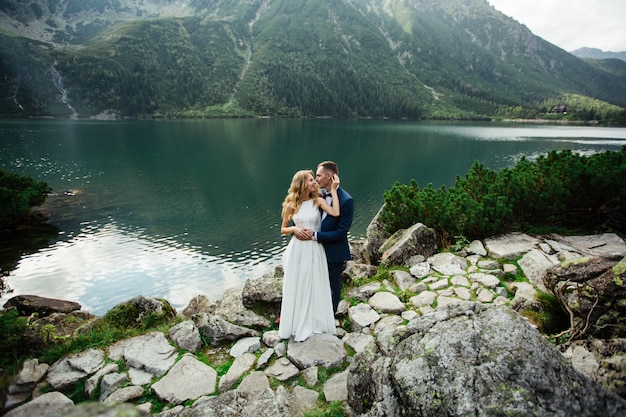 Couple de mariage sensuel debout sur la rive pierreuse du lac Sea Eye en Pologne.