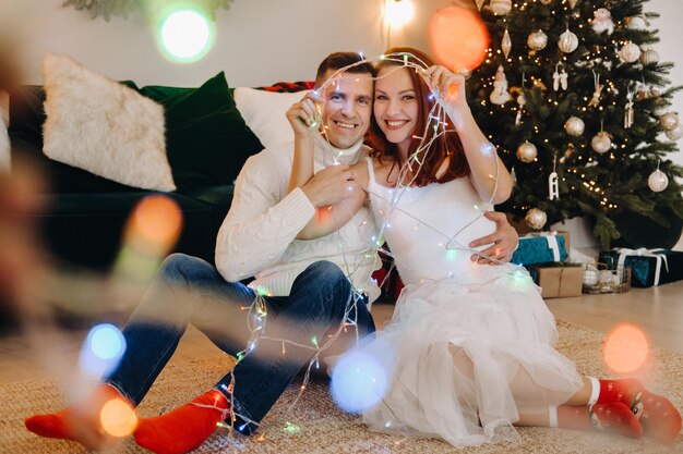 Un couple marié heureux est assis à la maison sur le sol près de l'arbre de Noël