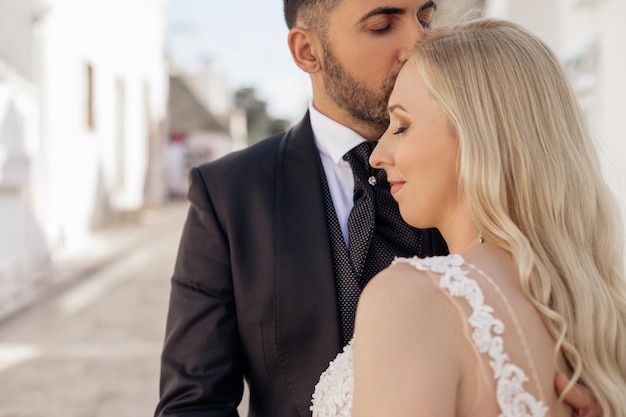 Couple marié jolie femme blonde bouclée mariée et homme barbu aux cheveux noirs marié debout ensemble s'embrasser doucement