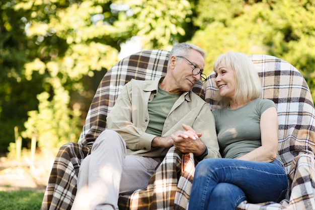 Couple marié senior aimant se reposer dans leur jardin à la campagne assis dans des chaises en osier et