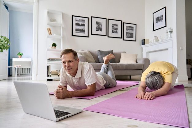 Couple mature en bonne santé regardant un cours de fitness yoga en ligne faisant de l'exercice à la maison