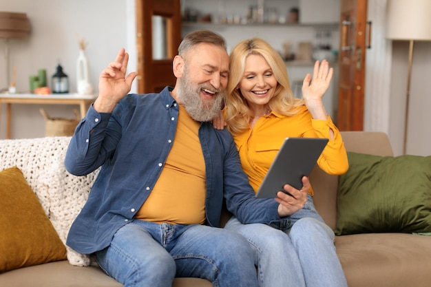 Un couple mature effectue un appel vidéo en utilisant une tablette en faisant des gestes à l'intérieur.