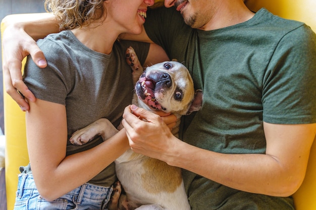 Couple méconnaissable s'embrassant avec un chien à la maison. Vue de dessus horizontale caressant l'animal de compagnie de bouledogue sur le canapé.