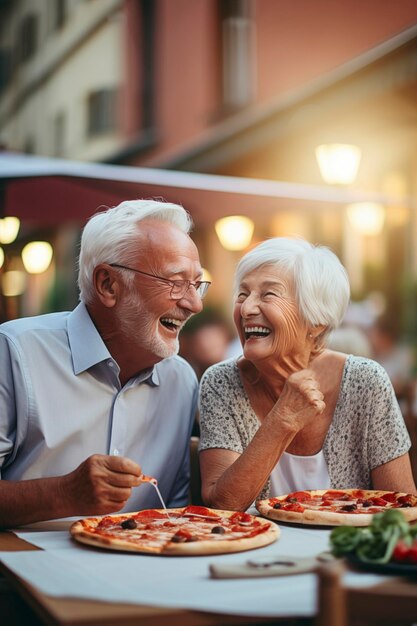 Un couple de messieurs âgés aux cheveux blancs sourient en mangeant une pizza célébrant un anniversaire dans une pizzeria assis à l'extérieur concept de gens heureux