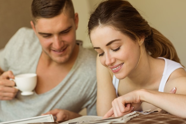 Couple mignon, lisant un journal au lit