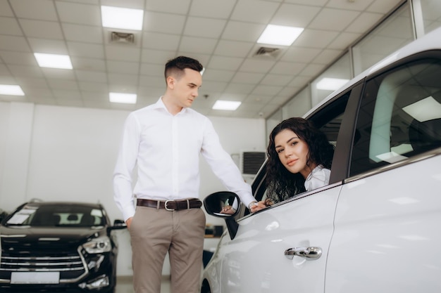 Un couple de milléniaux heureux prenant la clé de la voiture d'un vendeur d'automobiles assis à l'intérieur d'une automobile moderne au concessionnaire panorama Une jeune famille joyeuse achète un nouveau véhicule dans une salle d'exposition moderne