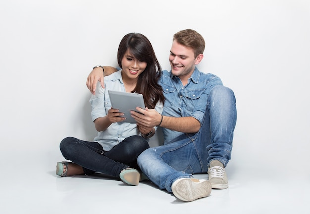 Couple mixte assis sur le sol tout en regardant quelque chose dans un tablet pc