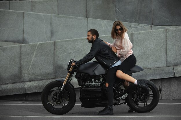 Couple de mode assis sur une moto, mur de pierre