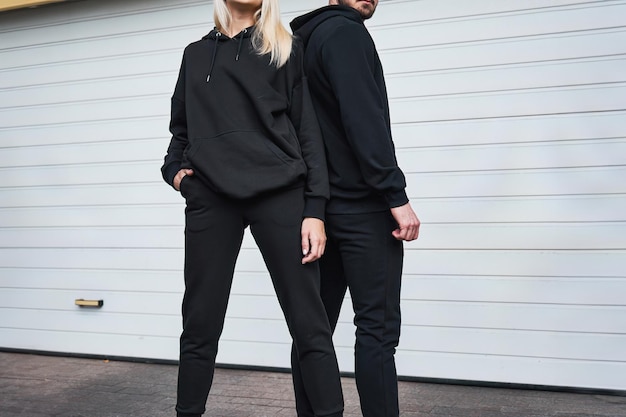 Un couple à la mode pose à l'extérieur dans des capuchons noirs pour un modèle de conception Un modèle de mode pour l'impression et l'image de marque Un style de street wear décontracté et élégant sans visage et sans logo visible