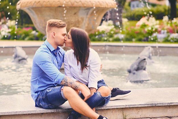 Un couple moderne attrayant à un rendez-vous pose sur la fontaine de la ville.