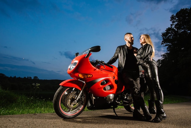 Couple de motards cool en vestes de cuir assis sur un vélo de sport rouge à l'extérieur