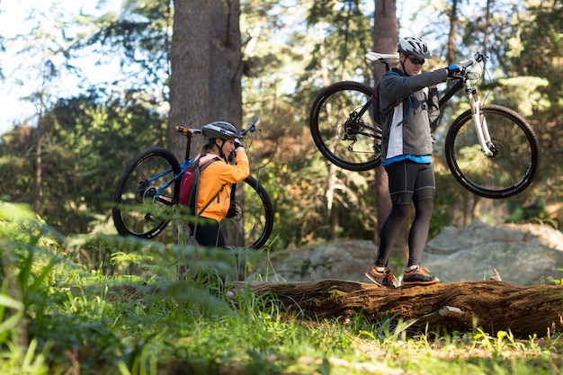 Couple de motards tenant leur vélo de montagne et marchant dans la forêt