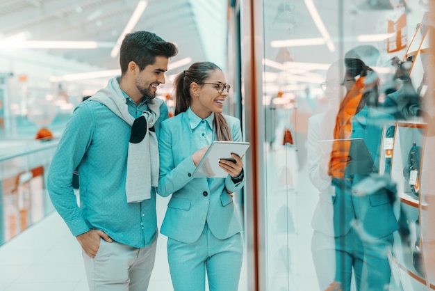 Couple multiculturel souriant habillé élégant en regardant la fenêtre commerçante dans le centre commercial.