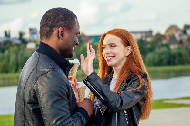 Couple multiethnique diversifié mangeant des glaces dans le parc d'automne de printemps