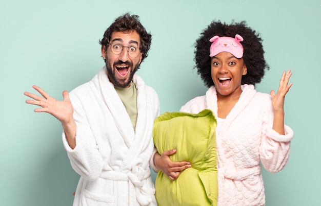 Un couple multiracial d'amis se sentant heureux, excité, surpris ou choqué, souriant et étonné par quelque chose d'incroyable. pyjama et concept de maison