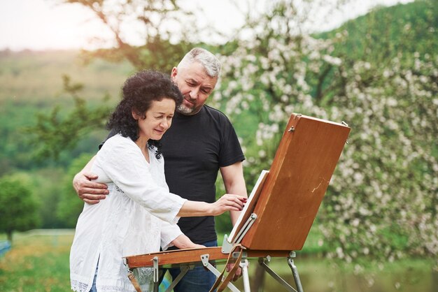 Un couple mûr a des jours de loisirs et travaille ensemble à la peinture dans le parc.