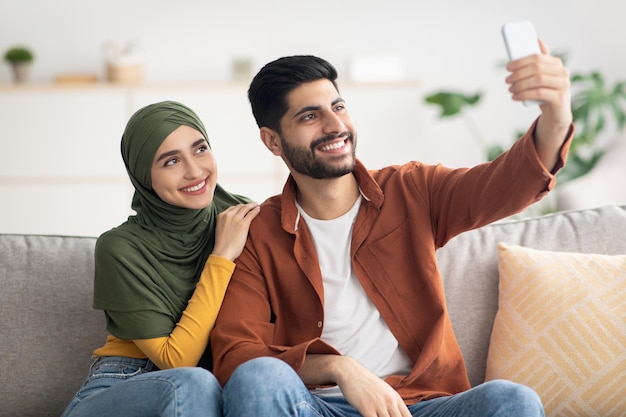 Couple musulman faisant selfie sur téléphone portable s'amusant à l'intérieur