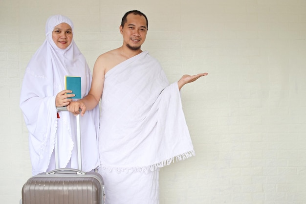 Couple musulman portant des vêtements blancs d'ihram prêt pour le Hajj ou la Omra, tenant un passeport et une valise whi