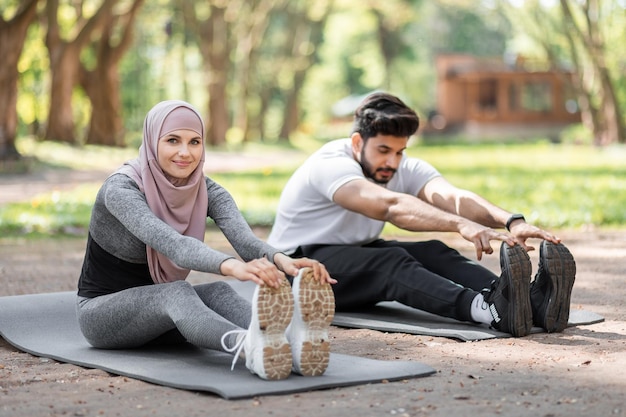 Couple musulman en vêtements de sport étirant les jambes à l'extérieur