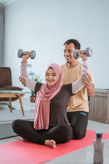 Couple de musulmans asiatiques exerçant et soulever des poids à la maison. mari aidant sa femme à s'entraîner