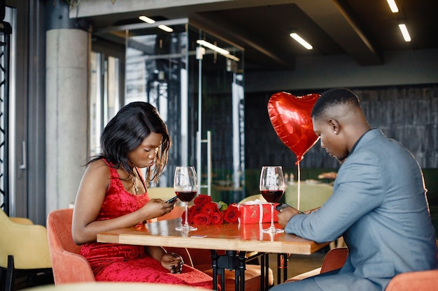 Un couple noir romantique assis dans un restaurant portant des vêtements élégants