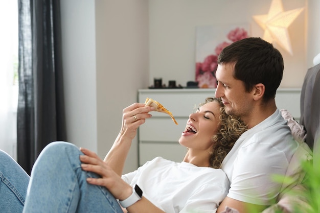Couple paresseux et heureux se détendre à la maison. Manger de la pizza et s'allonger sur le lit.