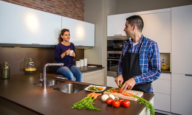 Couple parlant dans la cuisine pendant que le mari coupe des légumes pour préparer à manger